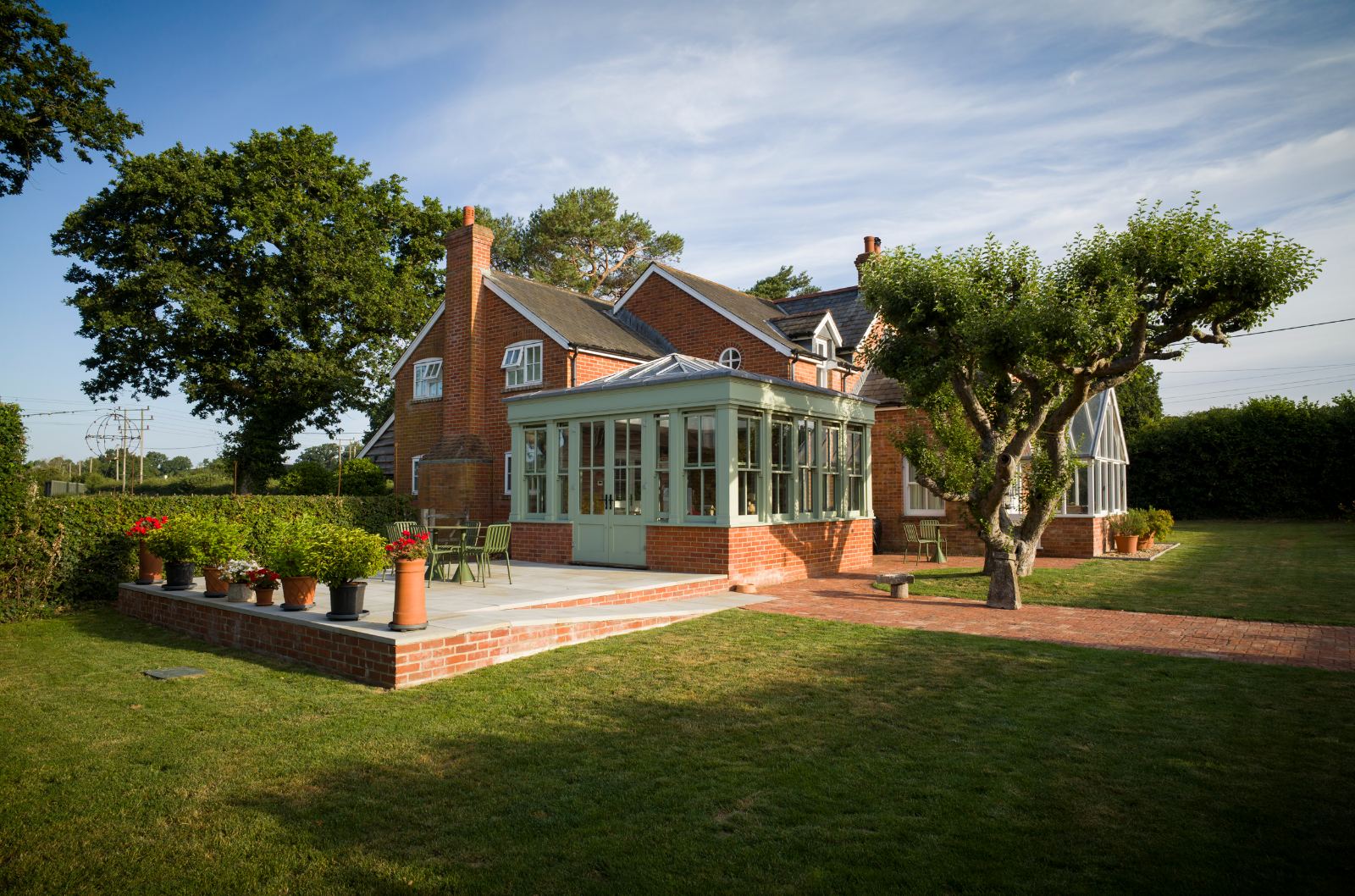 A finished Banks Landscapes garden: brick terrace and oak-framed orangery under a wide New Forest sky