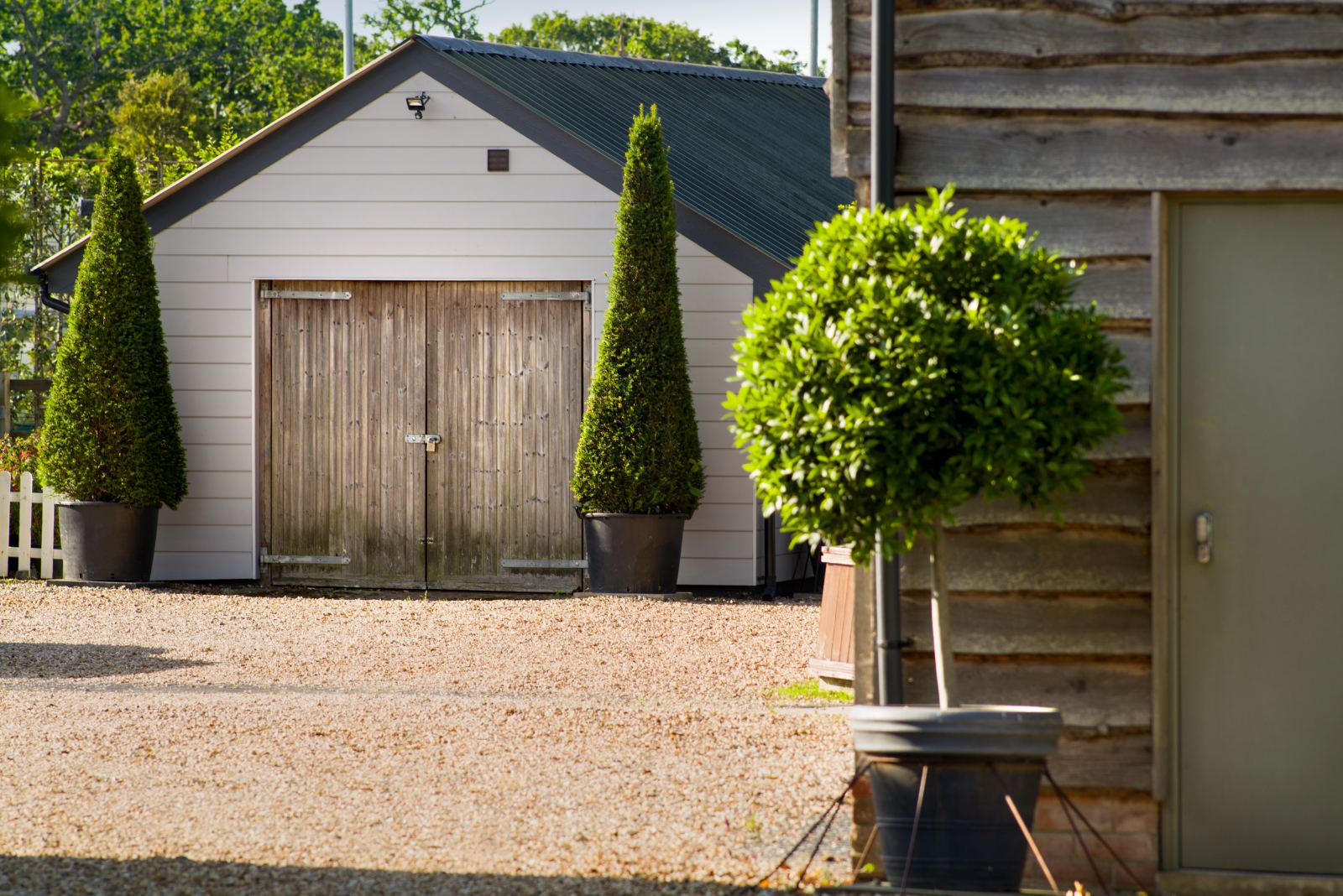 Clipped evergreens flanking timber barn doors on a gravelled yard
